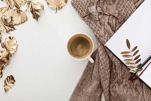 top view of knitted brown sweater, glasses, coffee, blank notebook and golden foliage on white background