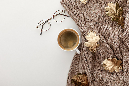 top view of knitted sweater, glasses, coffee and golden foliage on white background