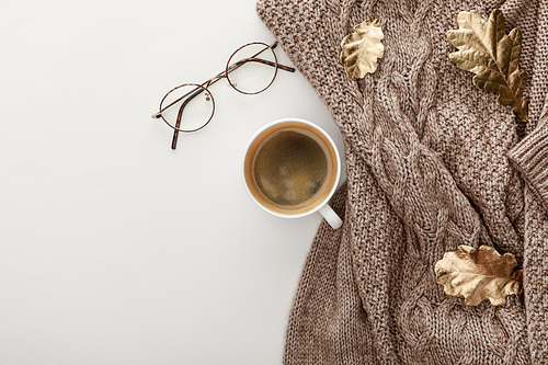 top view of knitted brown sweater, glasses, coffee and golden foliage on white background
