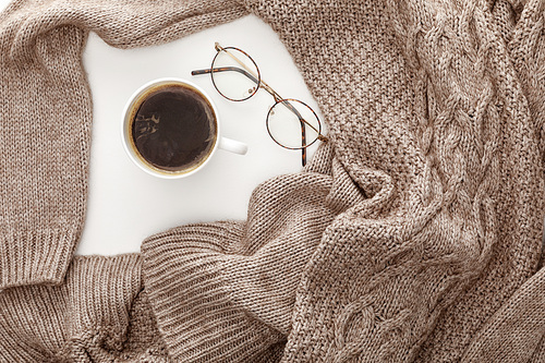 top view of knitted brown sweater, coffee and glasses on white background