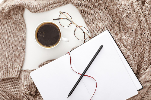 top view of empty notebook, knitted brown sweater, coffee and glasses on white background
