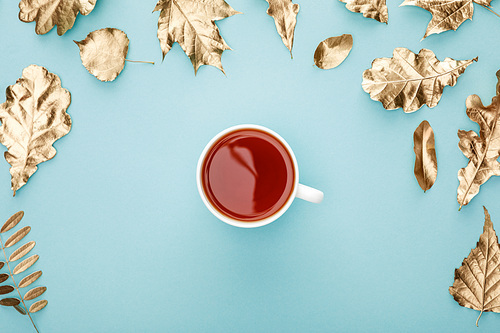 top view of warm tea in mug near golden foliage on blue background