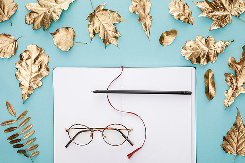 flat lay with autumnal golden foliage near blank notebook with glasses on blue background