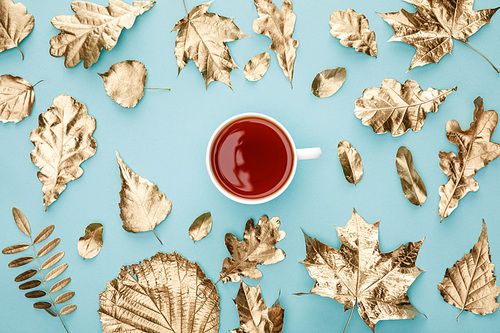 top view of tea in mug near golden foliage on blue background