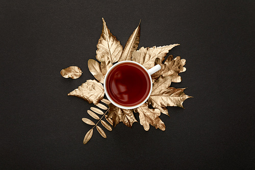 top view of tea in mug near golden foliage on black background
