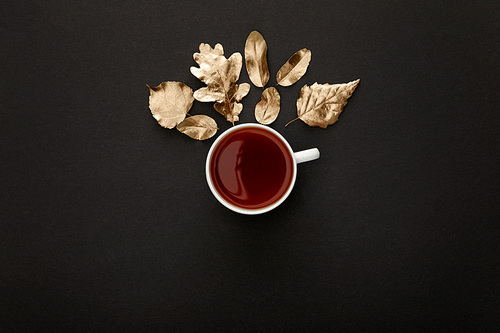 top view of hot tea in mug near golden foliage on black background