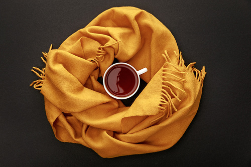 top view of tea in mug in cozy scarf on black background