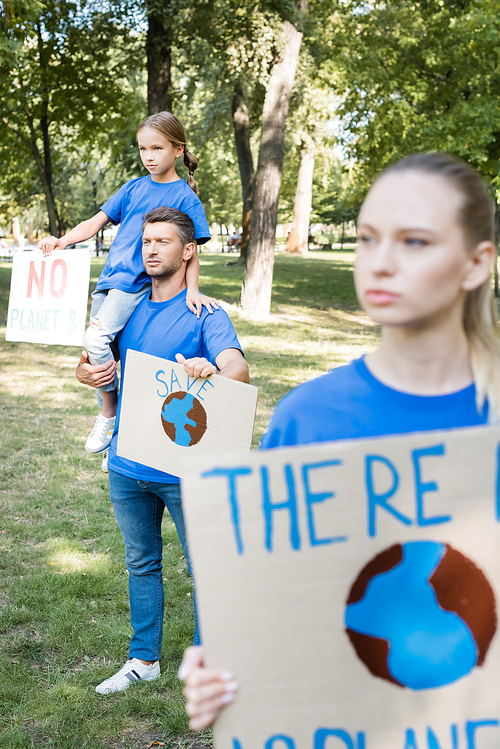 girl sitting on fathers shoulder, and mother standing on blurred foreground while holding placards with there is no planet b inscription, ecology concept