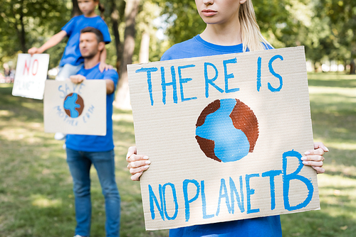 woman holding placard with globe and there is no planet b inscription near family with posters on blurred background, ecology concept