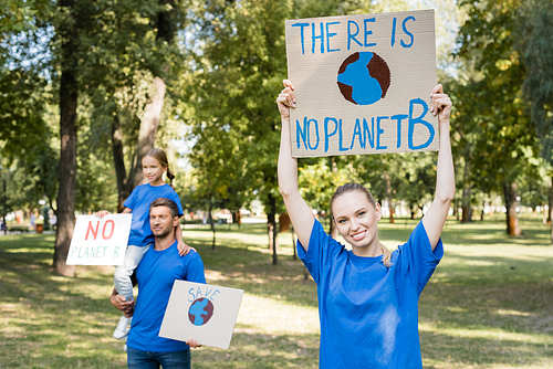 happy woman holding placard with there is no planet b inscription near husband and daughter with posters on blurred background, ecology concept