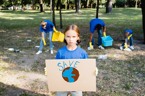 girl holding placard with globe and save inscription, while family collecting garbage on blurred background, ecology concept
