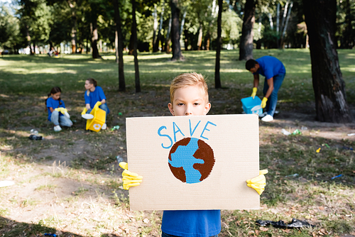 boy holding placard with globe and save inscription, while family collecting plastic waste on blurred background, ecology concept
