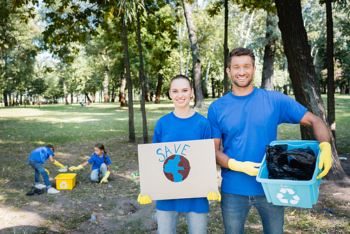couple holding placard with globe, save inscription, and rubbish container, while children collecting waste on blurred background, ecology concept