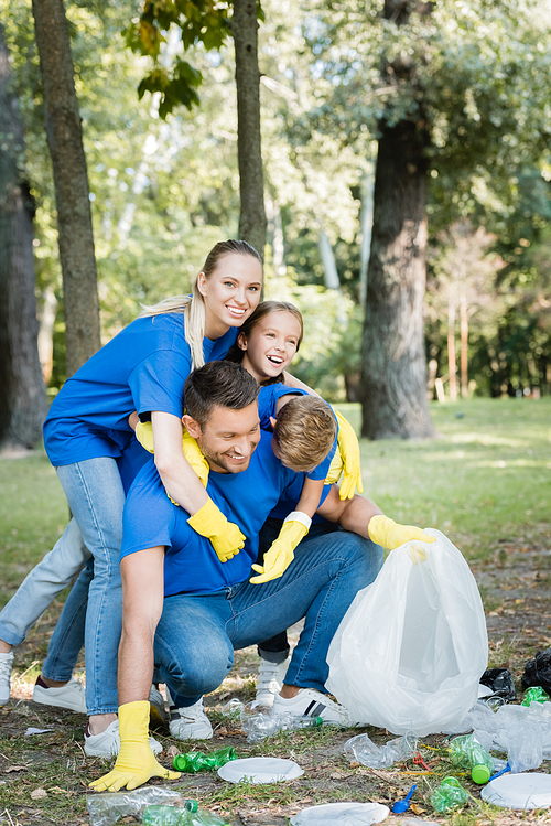 happy family embracing father while collecting plastic rubbish in forest, ecology concept