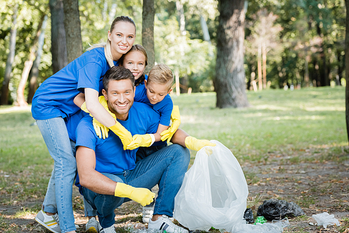 cheerful family embracing father holding recycled bag in forest, ecology concept