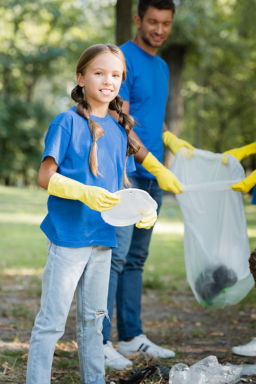 girl holding plastic plate and  near father with recycled bag on blurred background, ecology concept