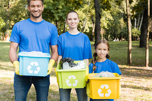 smiling family holding containers with recycling symbols, full of plastic waste, ecology concept