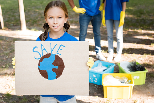girl holding placard with globe and save inscription, and parents near rubbish containers on blurred background, ecology concept