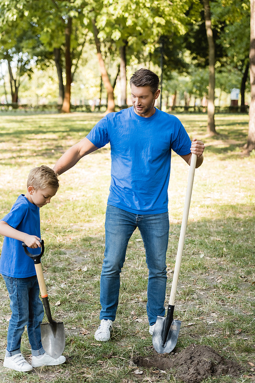 father and son digging ground in forest with shovels, ecology concept