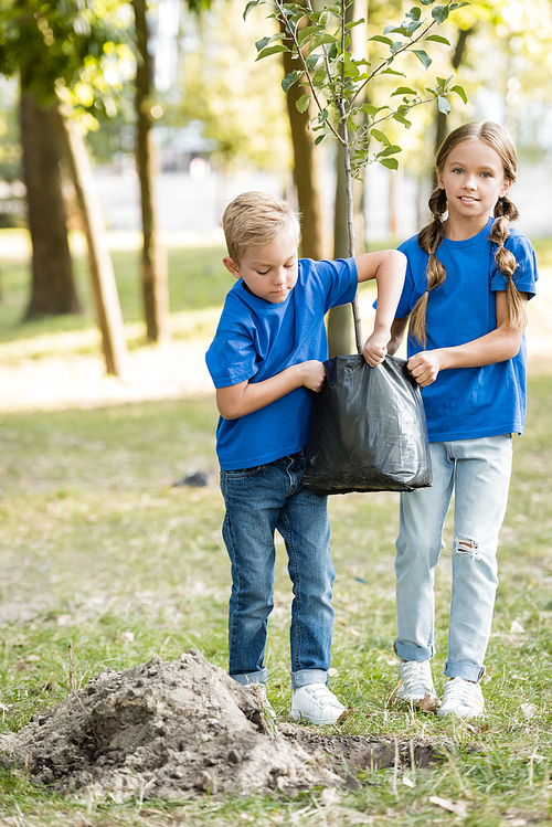 brother and sister carrying young seedling in park, ecology concept