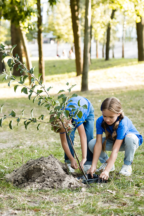 mother and daughter planting young tree in forest, ecology concept