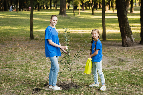 happy mother and daughter planting young tree in forest, ecology concept