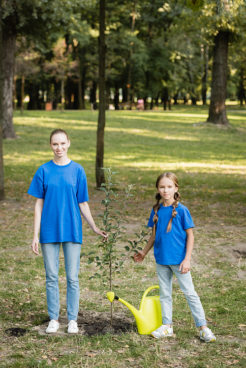 happy mother and daughter  while standing near young planted tree, ecology concept
