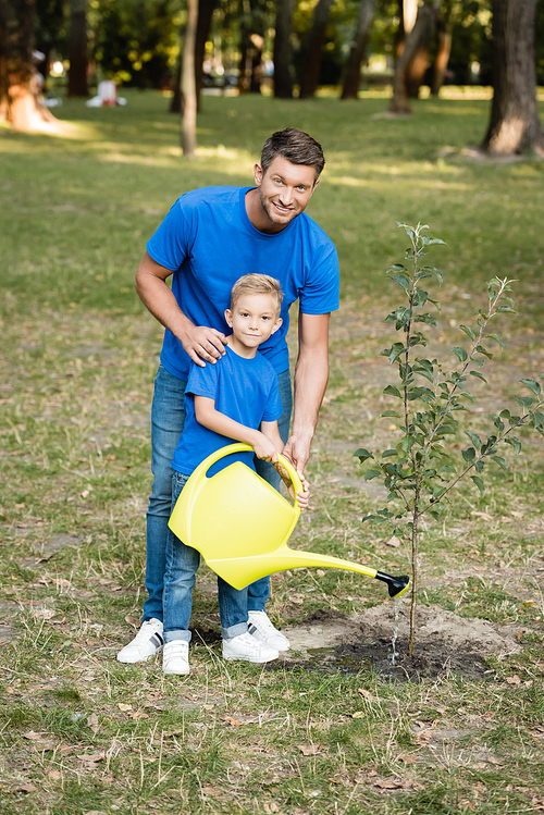 boy  while watering planted young tree near smiling father, ecology concept