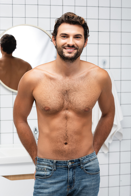 Muscular man in jeans smiling at camera in bathroom