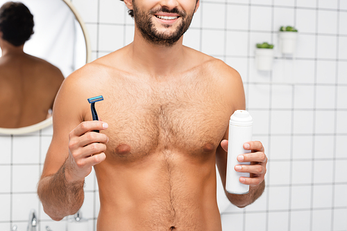 Cropped view of smiling shirtless man holding razor and shaving foam in bathroom