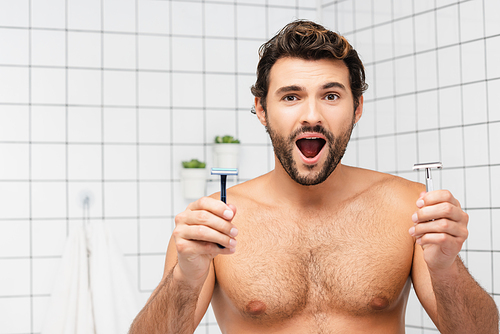 Excited shirtless man  while holding razors in bathroom