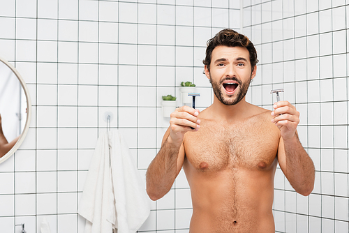 Excited shirtless man holding razors in bathroom
