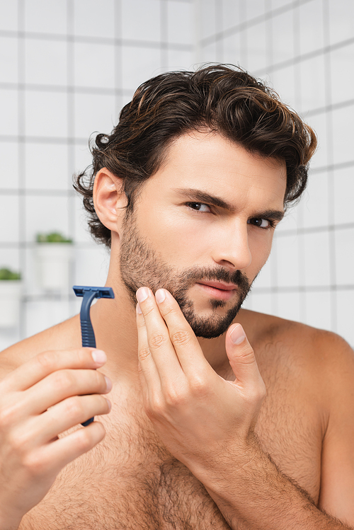 Bearded man holding razor and  in bathroom