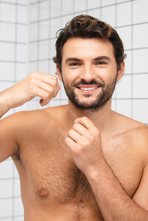 Shirtless man smiling at camera while holding dental floss in bathroom