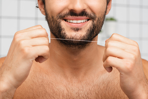 Cropped view of bearded man smiling while holding dental floss in bathroom