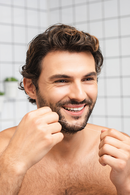Smiling man holding dental floss and looking away in bathroom