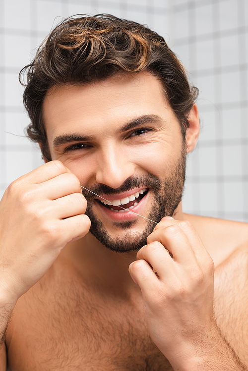 Smiling shirtless man using dental floss while  in bathroom