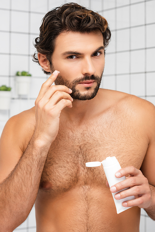 Shirtless man applying cosmetic cream and  in bathroom