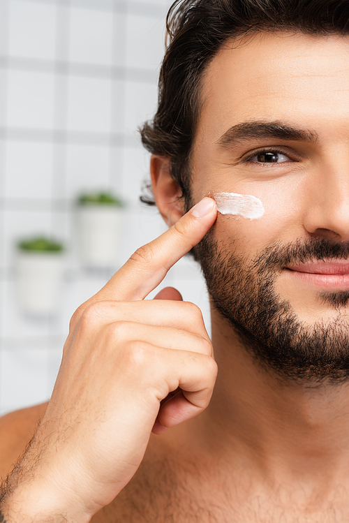 Cropped view of smiling man applying cosmetic cream on cheek