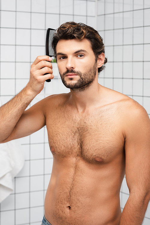 Muscular man combing hair and  in bathroom