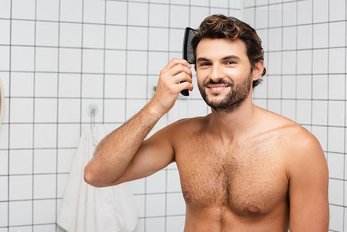 Smiling muscular man combing hair in bathroom