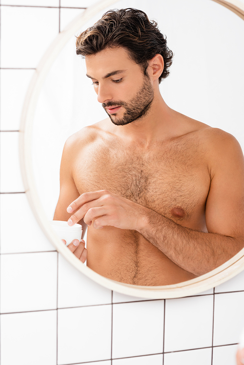 Shirtless man holding jar with cosmetic cream in bathroom