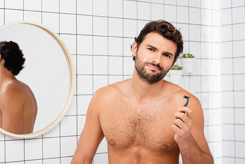 Shirtless man with wound on cheek  while holding razor in bathroom