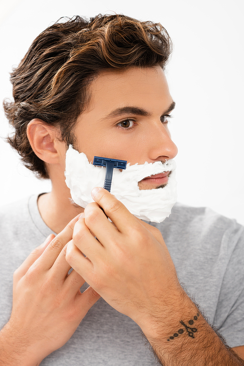 Young man with foam on face shaving with razor isolated on grey