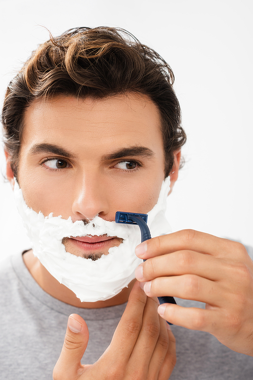 Young man with foam on face shaving with disposable razor isolated on grey