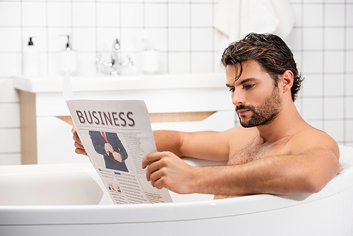 Bearded man reading business newspaper while taking bath