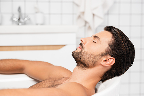 Bearded man taking bath with closed eyes at home