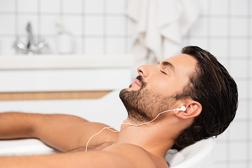 Bearded man listening music in earphones in bath
