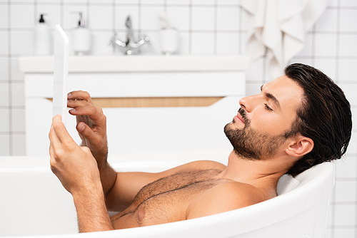 Young man using digital tablet while taking bath