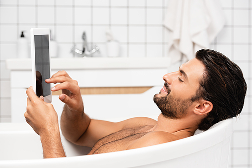 Smiling man using digital tablet with blank screen while taking bath at home